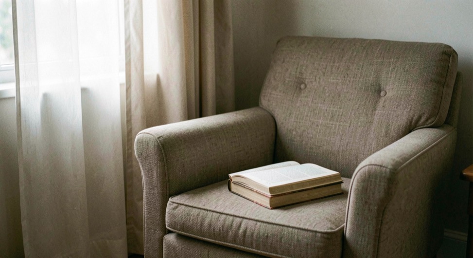 Calm reading corner with an armchair, a closed book and a window with sheer curtains, no devices in sight